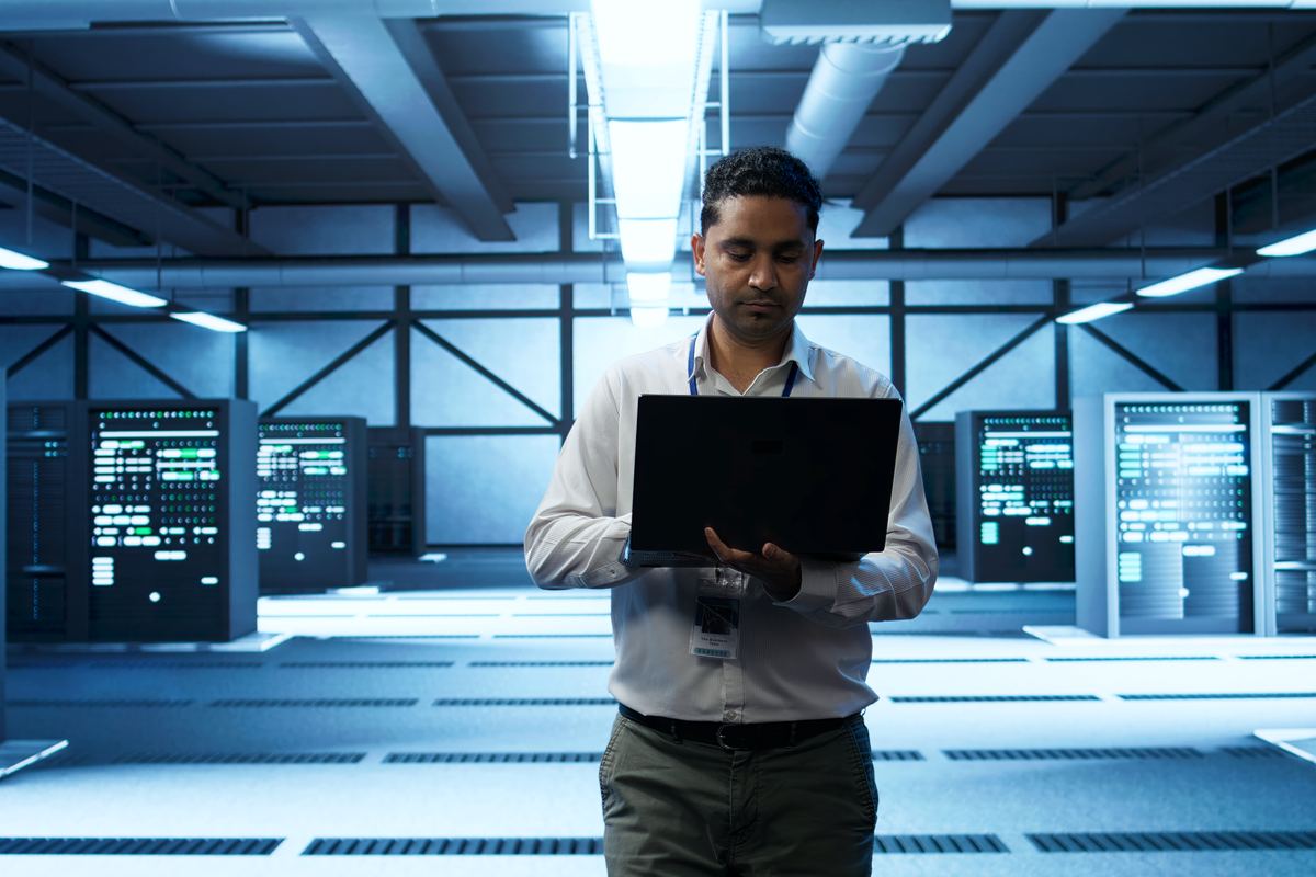 Technician working on a laptop between server racks